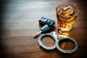 handcuffs next to a glass of alcoholic drink and car keys